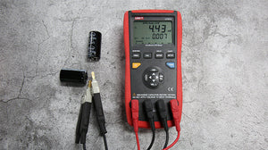 UNI-T UT612 Digital LCR Meter – 20000 Count, 100Hz–100kHz, L/C/R/DCR/Q/D/θ/ESR, Series/Parallel, Auto Range, USB, SMD Test Clamp, Handheld Bridge - with a red and black handheld body, measuring a capacitor with test clips, showing 4.43 mF and 0.007 on the digital display.