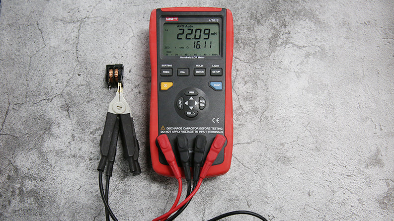UNI-T UT612 Digital LCR Meter – 20000 Count, 100Hz–100kHz, L/C/R/DCR/Q/D/θ/ESR, Series/Parallel, Auto Range, USB, SMD Test Clamp, Handheld Bridge - with a red and black handheld body, displaying 22.09 mH and 16.11, connected to an SMD test clamp holding a small component.