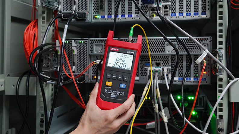 UNI-T UT693D Optical Multimeter – Fiber Power Meter (-70~10DBM, 800–1700nm) + 10mW VFL, FC/SC/ST, InGaAs, IP65, Optical Power Meter & Fault Locator - held in a hand, showing a red casing, buttons, and a digital display reading -36.08 dBm connected to a fiber optic cable.