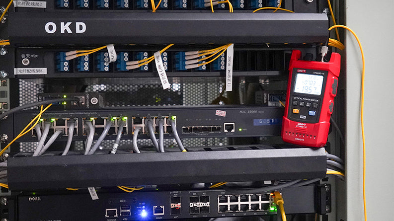 UNI-T UT695D-10 Optical Multimeter – Fiber Power Meter (-70~3dBm, 800–1700nm) + 10mW VFL + LAN Cable Test + Flashlight, FC/SC/ST, Rechargeable - a red handheld device with a digital display showing -0103 and 1957, connected to fiber optic cables in a server rack.