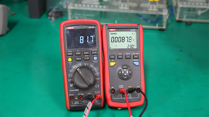 UNI-T UT701 Single-Function Temperature Calibrator – Thermocouple (J/K/T/E/R/S/B/N/W) & RTD Source, mV / Resistance, Ramp & Step - next to a multimeter on a green surface, showing temperature readings of 87.8°C and 81.7°C on their respective displays.
