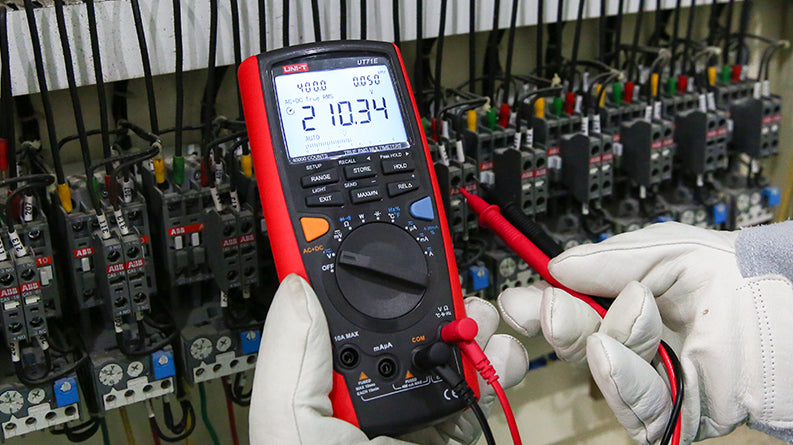 UNI-T UT71E High-Precision Intelligent True RMS Digital Multimeter – 40000 Count, AC/DC 1000V, 0.025% Accuracy, 400MHz, Temperature, USB, Bluetooth & Power Adapter - with a red and black casing, showing a digital display reading 210.34 V while held by gloved hands against a control panel.