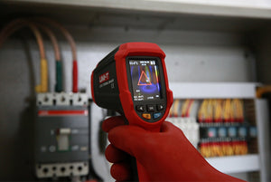 UNI-T UTI32 High Temperature Thermal Camera – 32×32, -20°C to 1000°C, 0.15°C - held by a gloved hand, showing a red and black pistol-grip body, control buttons, and a screen displaying thermal data.