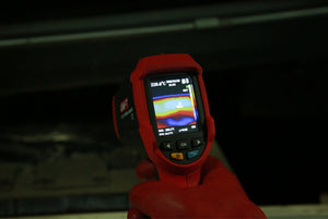 UNI-T UTI32 High Temperature Thermal Camera – 32×32, -20°C to 1000°C, 0.15°C - held in a gloved hand, showing a red casing, navigation buttons, and a screen displaying a thermal heat map and temperature.