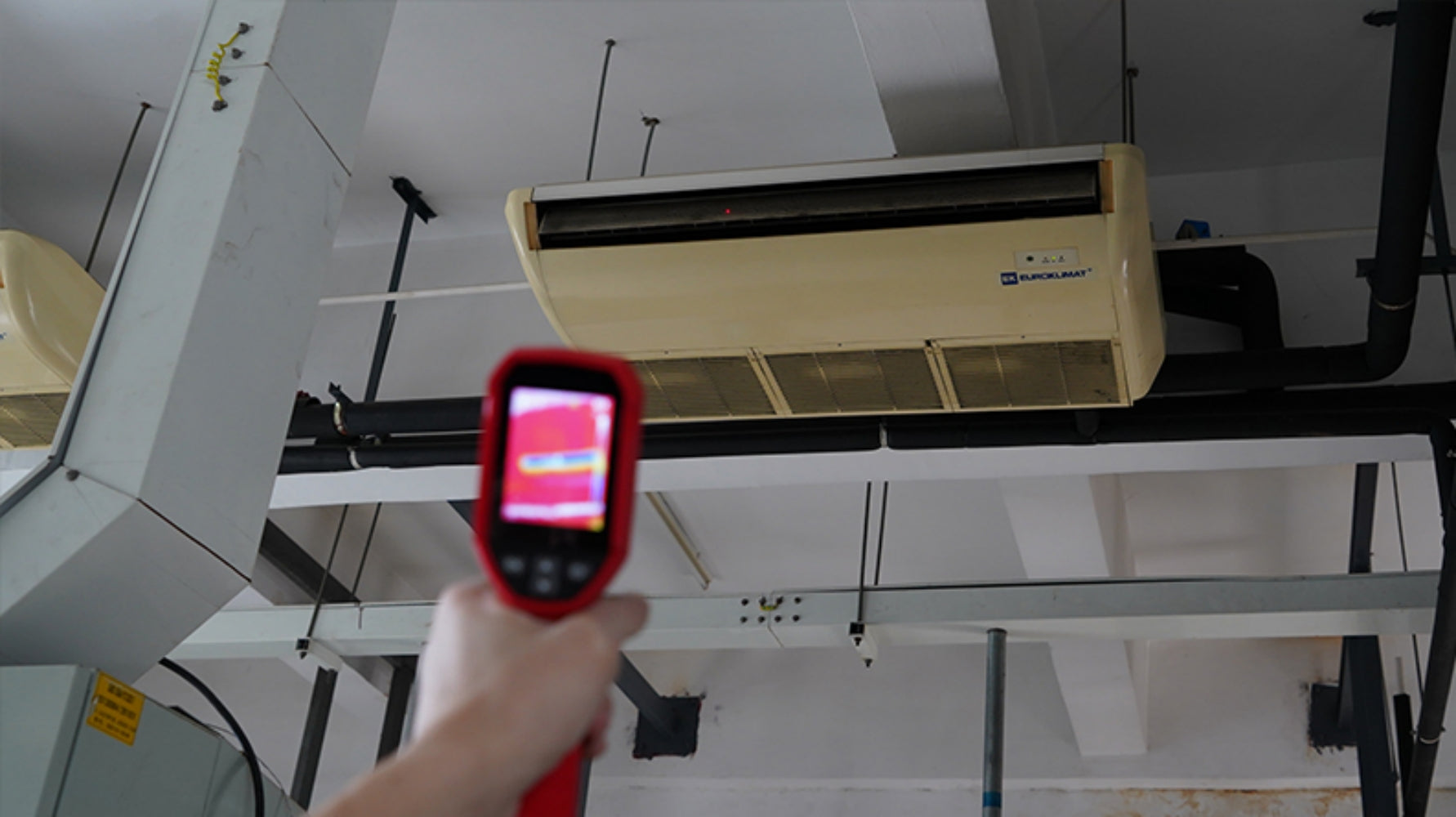 UNI-T UTI712S Cost-effective Thermal Camera – 120×90, -20°C to 400°C, ≤60MK - held in a hand, showing a red-and-black casing with a digital screen displaying a thermal heat map of an air conditioner.
