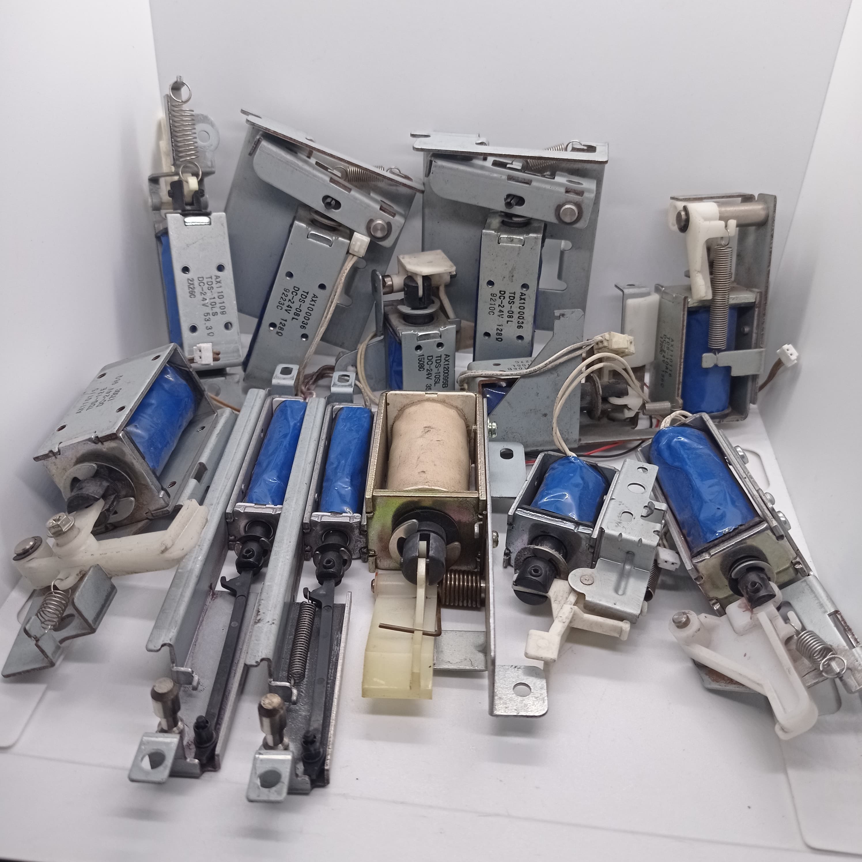 Used 1 Piece DC Solenoid Electromagnet In Mix Shape - a collection of various metal and blue plastic DC solenoid actuators with springs and levers.