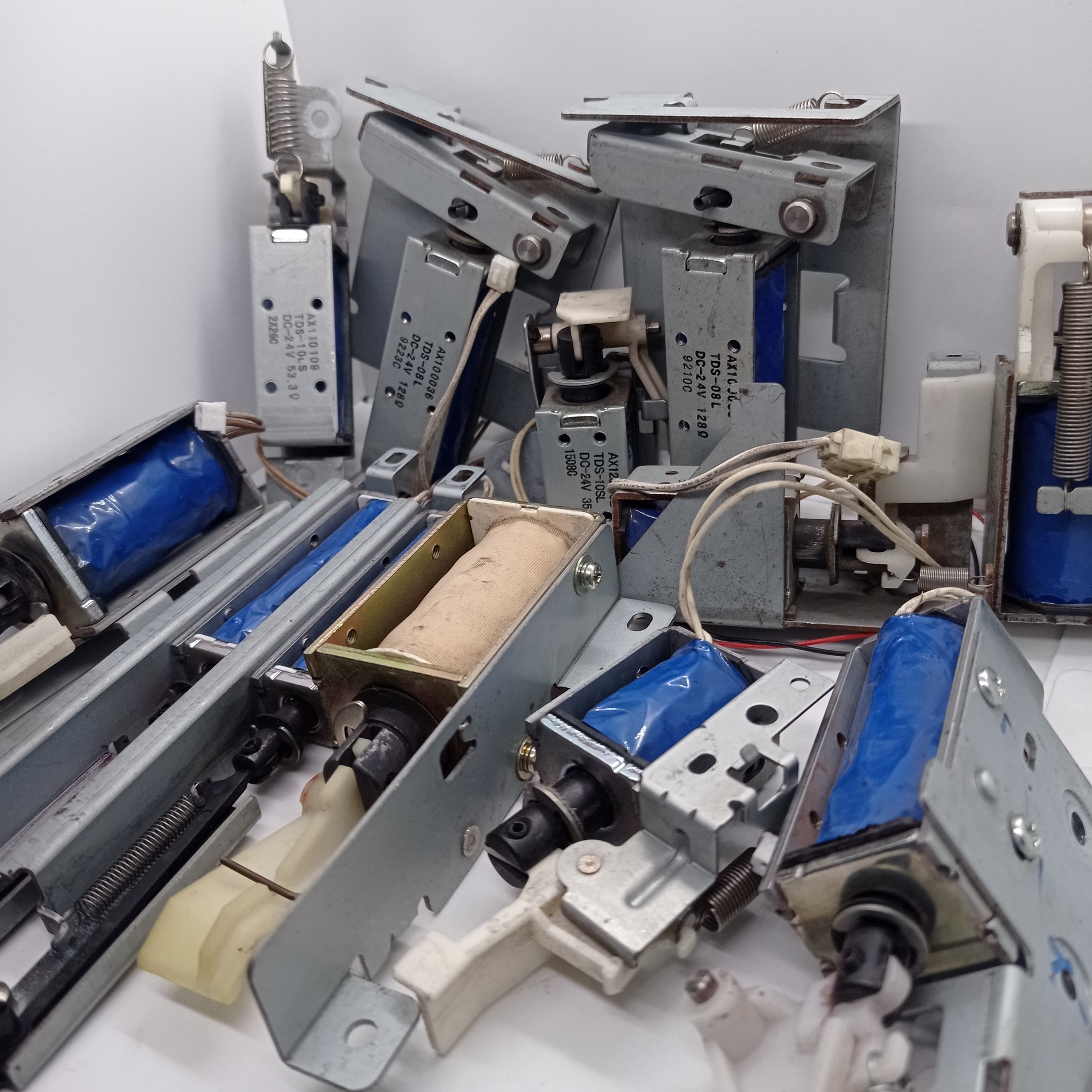 Used 1 Piece DC Solenoid Electromagnet In Mix Shape - a collection of various metal DC solenoid electromagnets with blue and tan coils and springs.