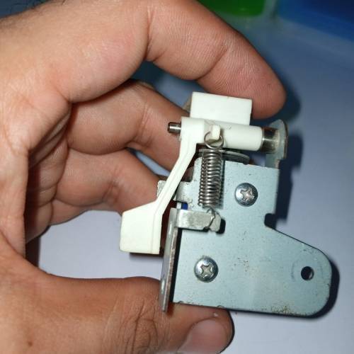 Used 1 Piece DC Solenoid Electromagnet In Mix Shape - a close-up of a metal and white plastic solenoid mechanism with an attached tension spring.