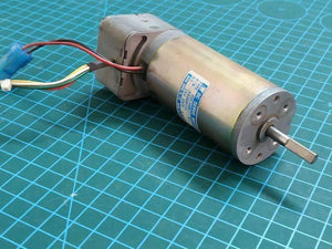 Used DC Servo Motor With Encoder High Speed 24V DC DSE38BE27-001IN Pakistan - a silver cylindrical motor with a shaft and a wired connector, resting on a green cutting mat.