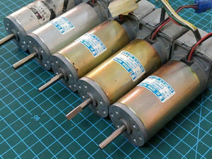 Used DC Servo Motor With Encoder High Speed 24V DC DSE38BE27-001IN Pakistan - five cylindrical gold and silver metal motors with shafts and attached wire harnesses on a cutting mat.