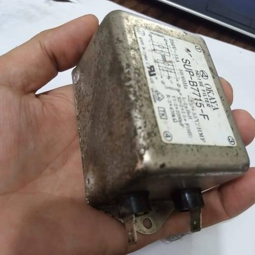 Used Noise Filter EMI Filter Anti-Interference Noise Signal Filtration Single Phase Mains Filter 125V 250V - a metallic, rectangular Okaya SUP-B7715-F unit held in a hand, featuring two bottom-mounted electrical terminals.