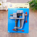 VARIED CF-5881 35mm Aluminum Alloy Table Bench Clamp Vise Multi-functional Bench Vise Table Screw Vise for DIY Craft Mold Fixed Repair Tool - shown in its blue and yellow retail packaging with two red-tipped adjustment handles.