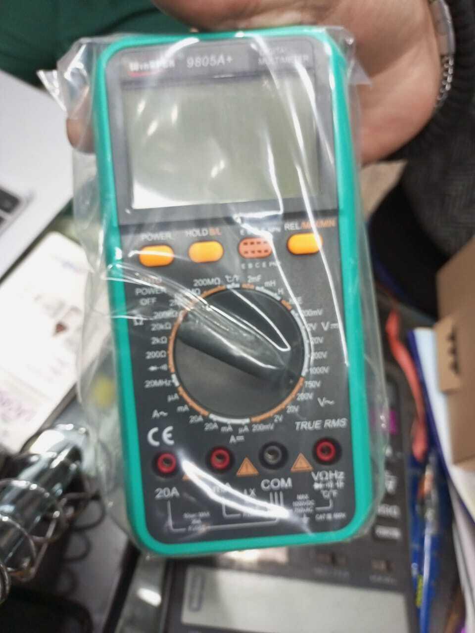 VC9805A+ Digital Multimeter - in green plastic casing, shown inside a clear protective plastic bag with a rotary dial, buttons, and input ports visible.