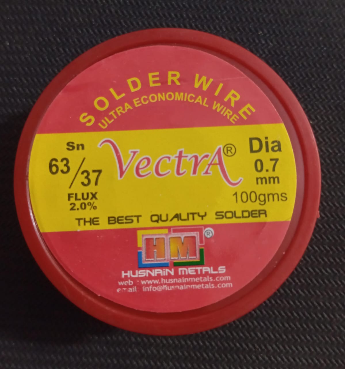 Vectra Solder Wire 100GRM 0.7mm size - a round, red plastic container with a yellow label showing product specifications including 63/37 Sn composition.