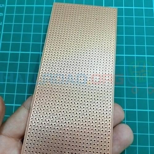 Veroboard Dotted Small Stripboard 6.5x14.5cm - a rectangular copper-colored circuit board with a grid of holes held in a hand over a green cutting mat.