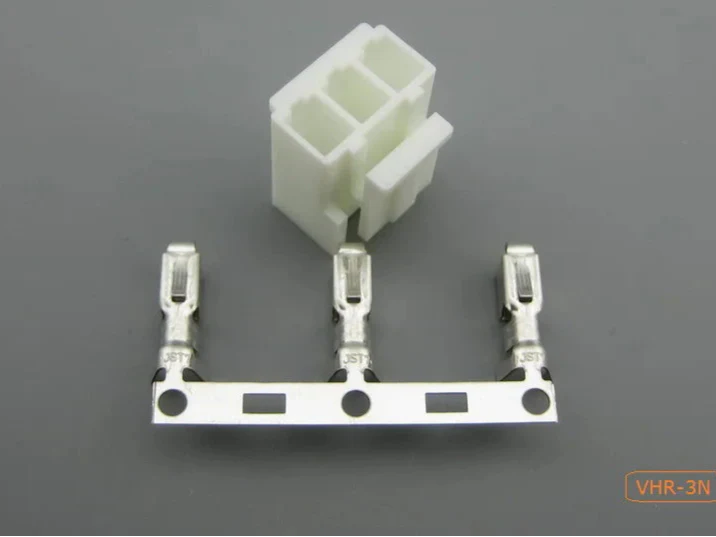 VHR Male and Female Connector Housing + THEMBEL , 3.96mm Pitch, 3 Way - a white 3-way plastic housing and three metal crimp terminals arranged in a row on a metal strip against a grey background.
