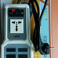 Wholesale HOPI HP-9800 Handheld Power Meter | Power Analyzer & LED Tester | Digilog.pk - a grey handheld tester with a universal power socket, red and black terminals, and six blank LCD screens, resting on its box.