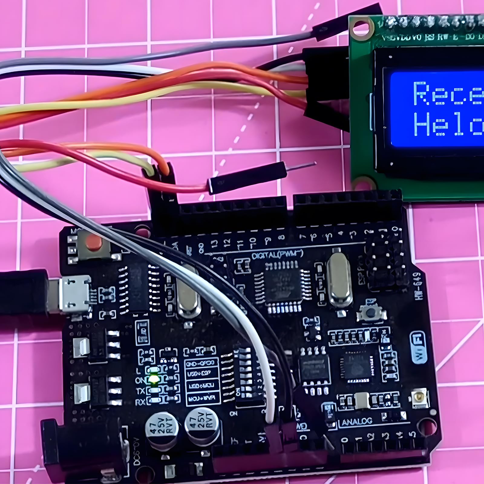 WiFi R3 ATMEGA328P + ESP8266 Development Board | Arduino UNO WiFi CH340G - + ESP8266 Development Board connected to an LCD screen displaying "Rece Helo" with multi-colored jumper wires on a pink grid mat.