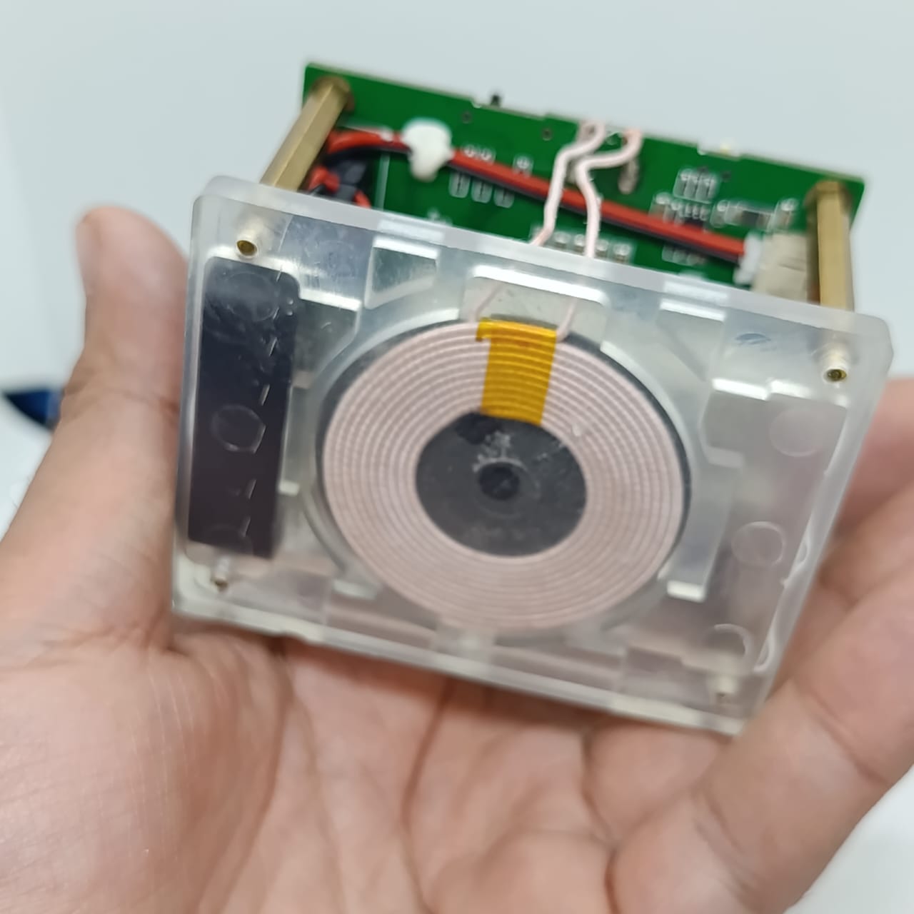 Wireless Charger Tester Smart Watches QI Wireless Charger Tester Voltage Current Load PCB Detector for Apple iWatch Galaxy Watch Wireless Chargers - a transparent square device held in a hand featuring a circular copper induction coil on a green circuit board with brass spacers.
