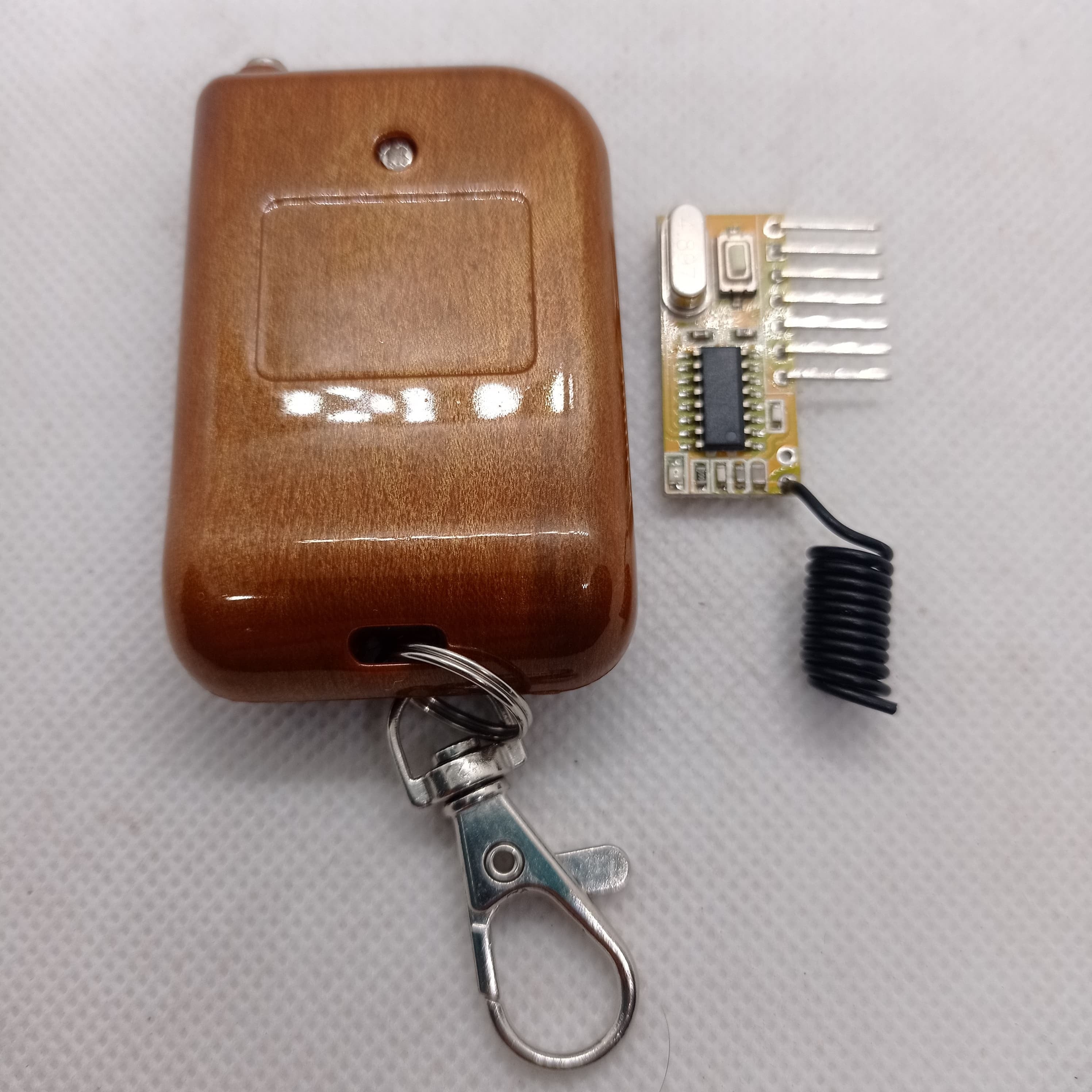 Without Battery 4 Channel Wireless Remote Control Kit RX12 RF Transmitter Receiver Module For Arduino Momentary Type - brown wooden-finish rectangular remote with a metal keychain and a small circuit board with a black coil antenna.